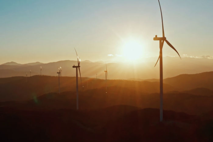 two wind turbines in the foreground and a sunset behind the mountains in the background