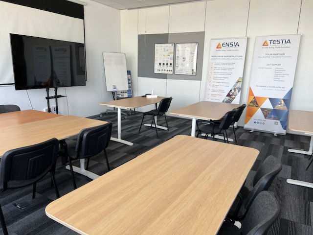Le centre de formation NDT de Madrid : salle lumineuse avec 10 chaises et 5 tables, un grand écran, un tableau blanc et des affiches informatives